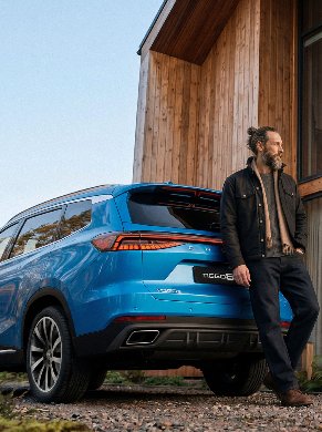 Man standing next to a blue SUV parked by a wooden building.