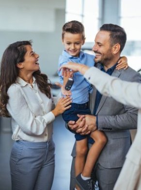 Family receiving car keys at a dealership, with a young boy smiling in his father's arms.