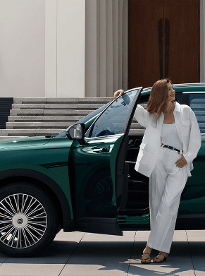 A woman in white stands by an open car door, a man walks towards the green SUV.