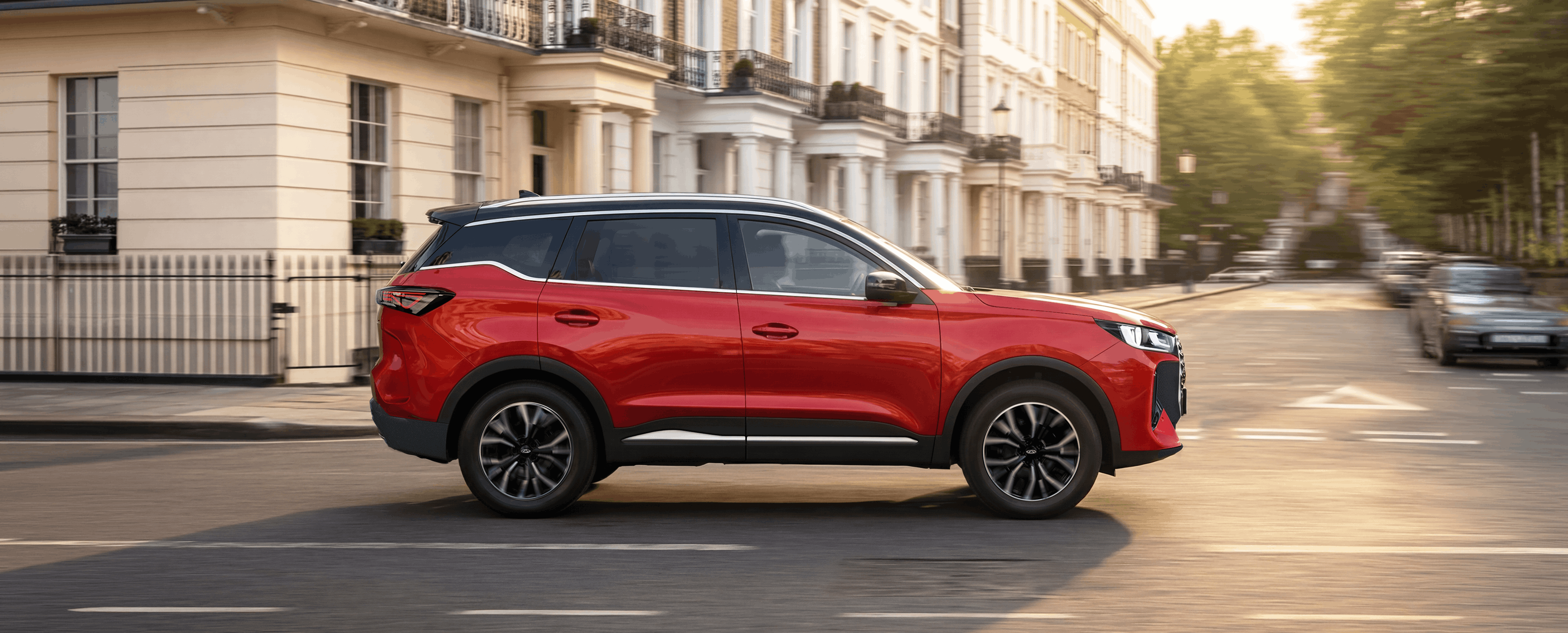 Red SUV driving on a street with terraced houses in the background.