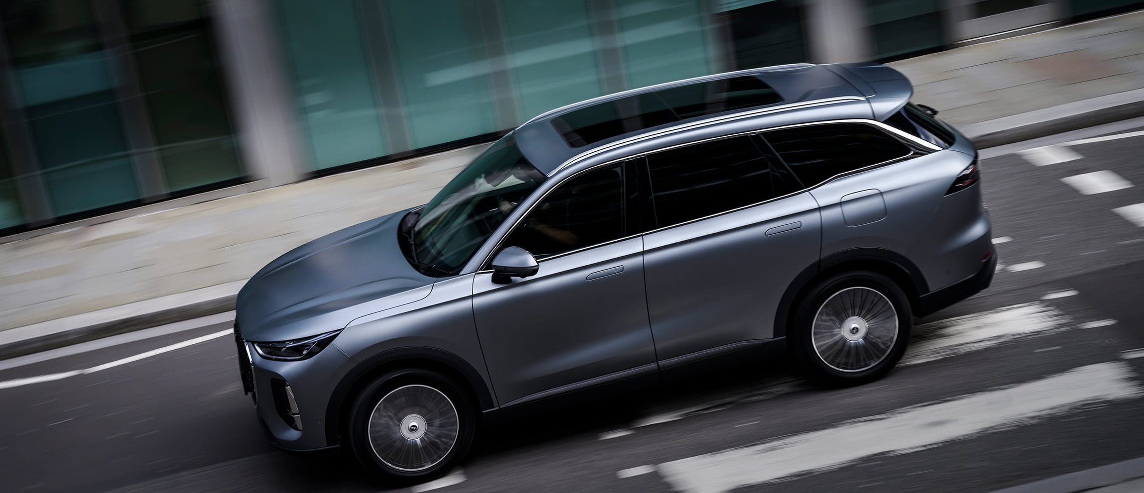 Sleek silver SUV driving on a city road, shot from above.