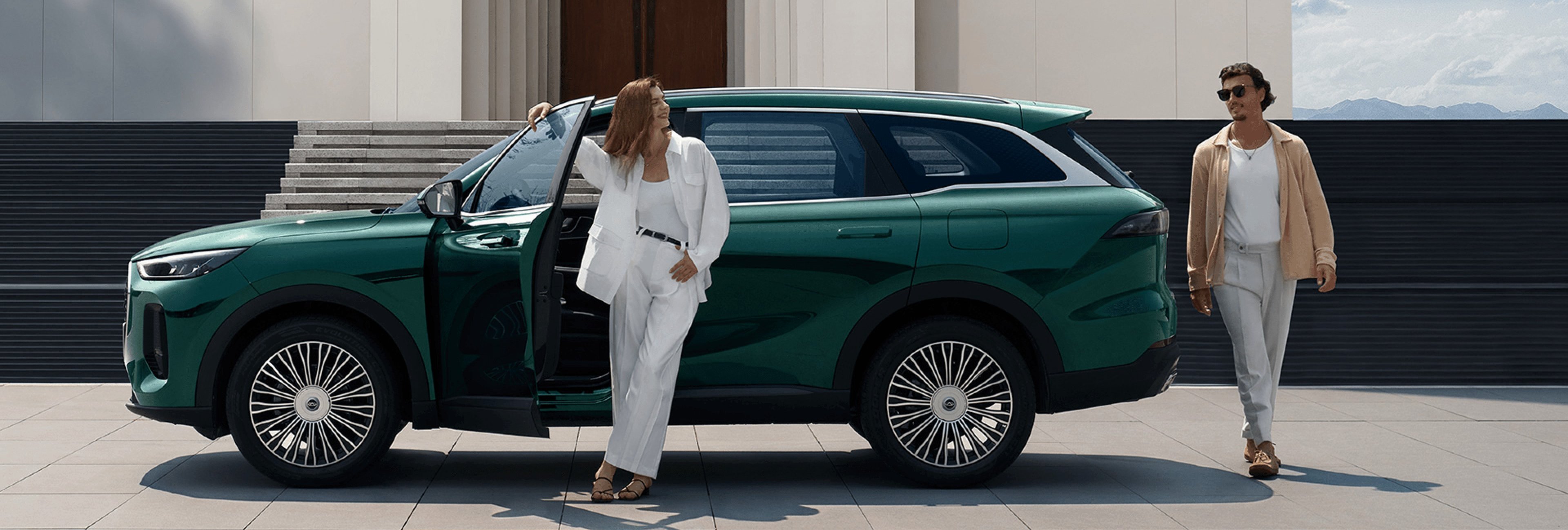 Woman leaning on a green SUV with a man walking nearby.
