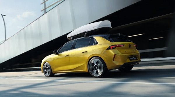 Yellow hatchback car with a roof box driving on a road.