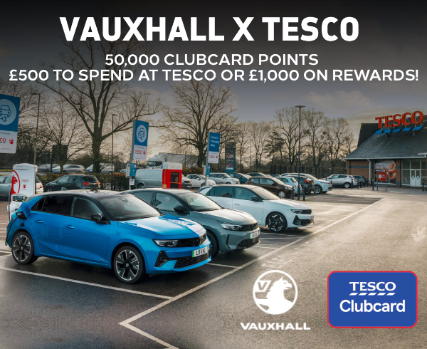 Cars parked at electric charging stations in a Tesco car park with Vauxhall and Tesco logos.
